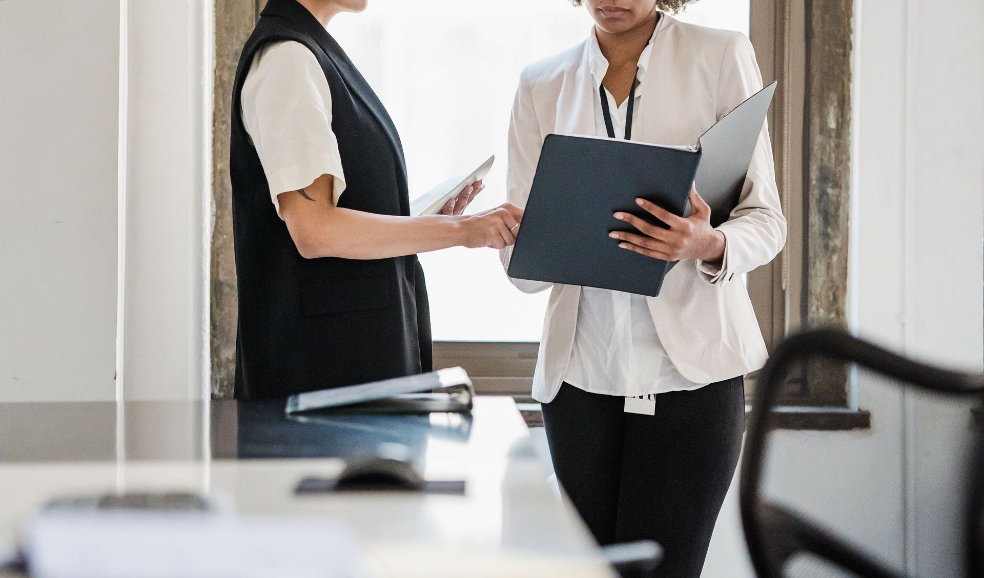 Two businesswomen discussing documents in a modern office setting.